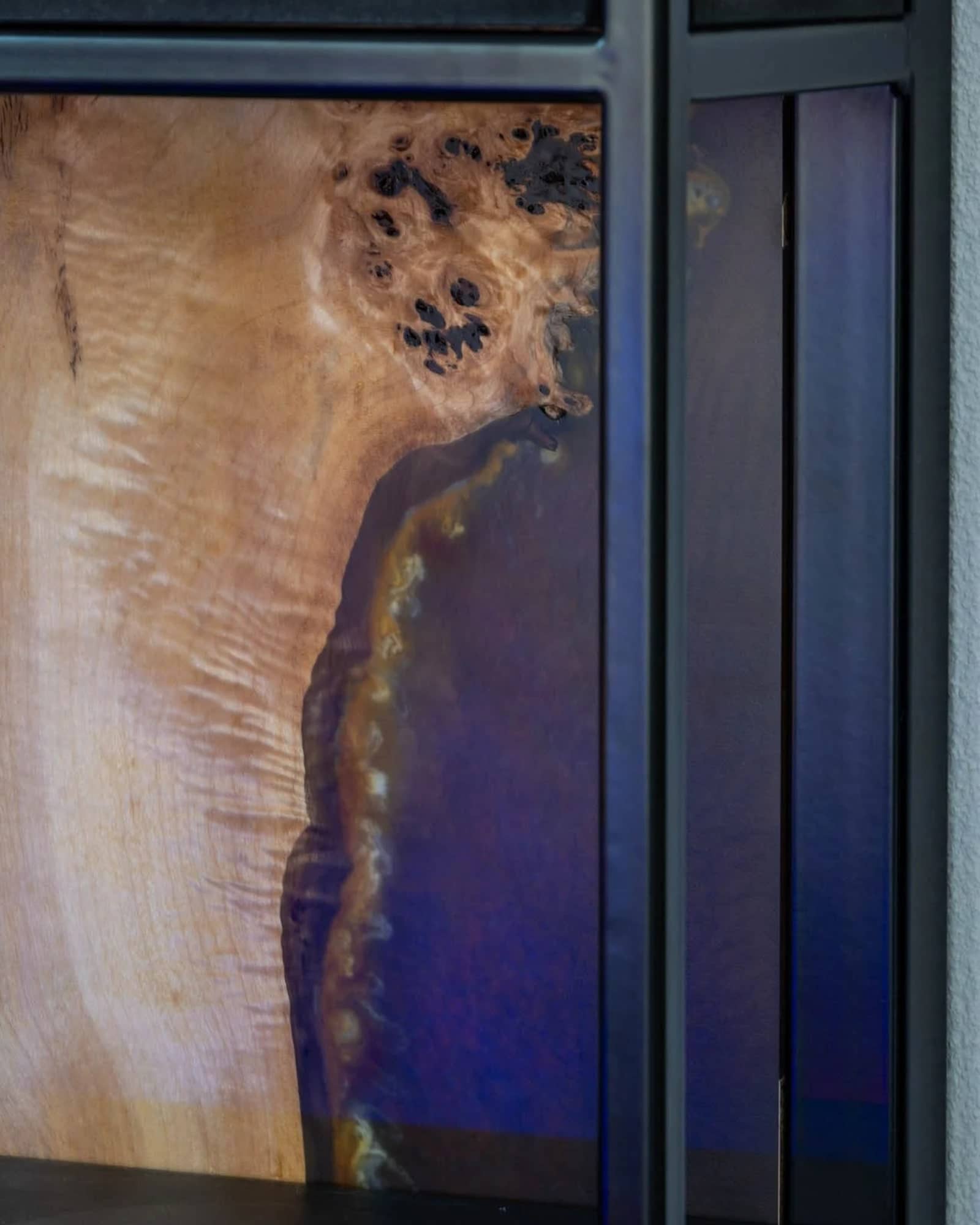 Platte aus hellem Maserholz mit blau-violettem Epoxidharz in einem schwarzen Metallrahmen.