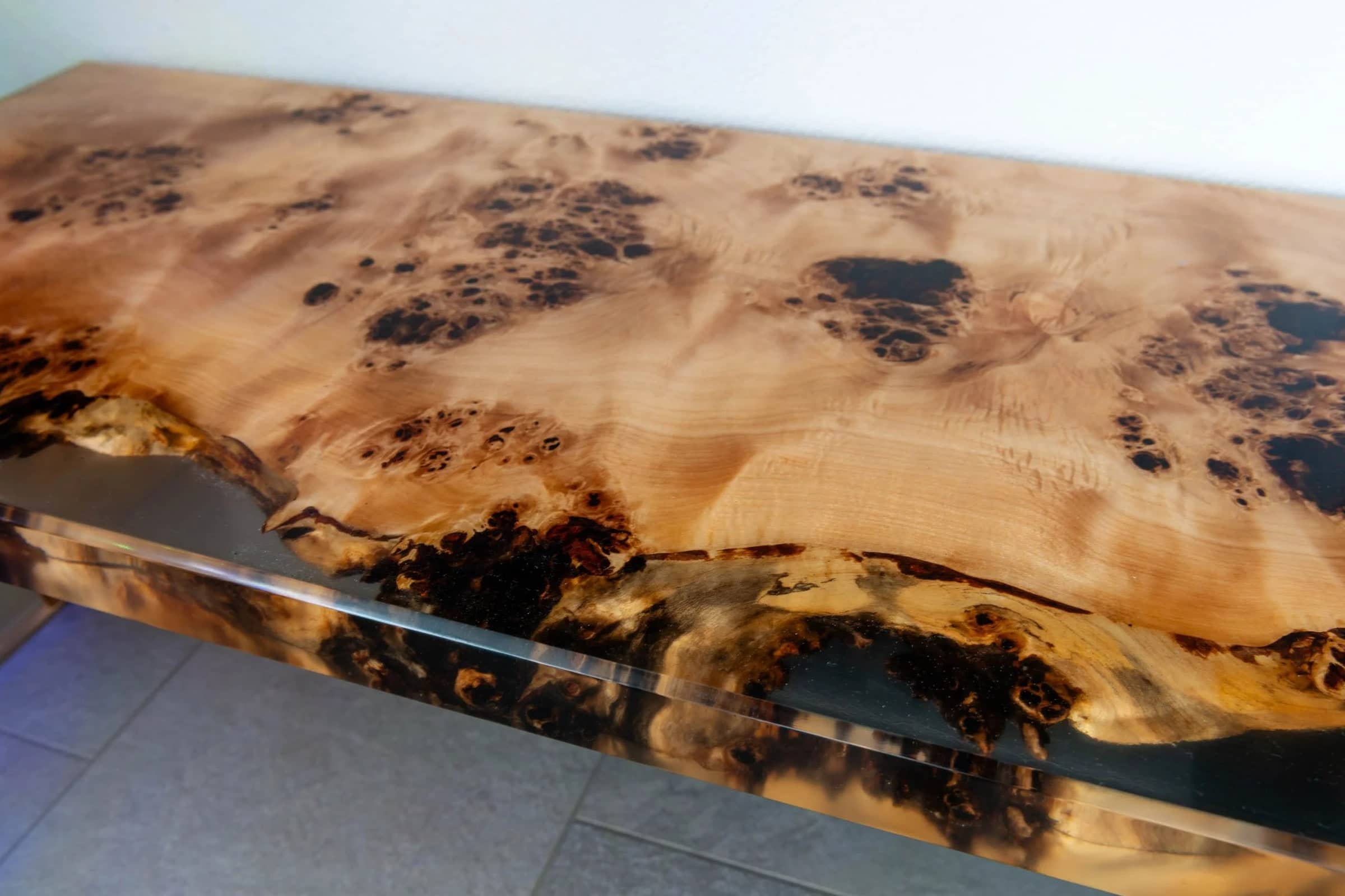 Tischplatte aus Maserholz mit einer Naturkante, die in klarem Epoxidharz eingegossen ist.