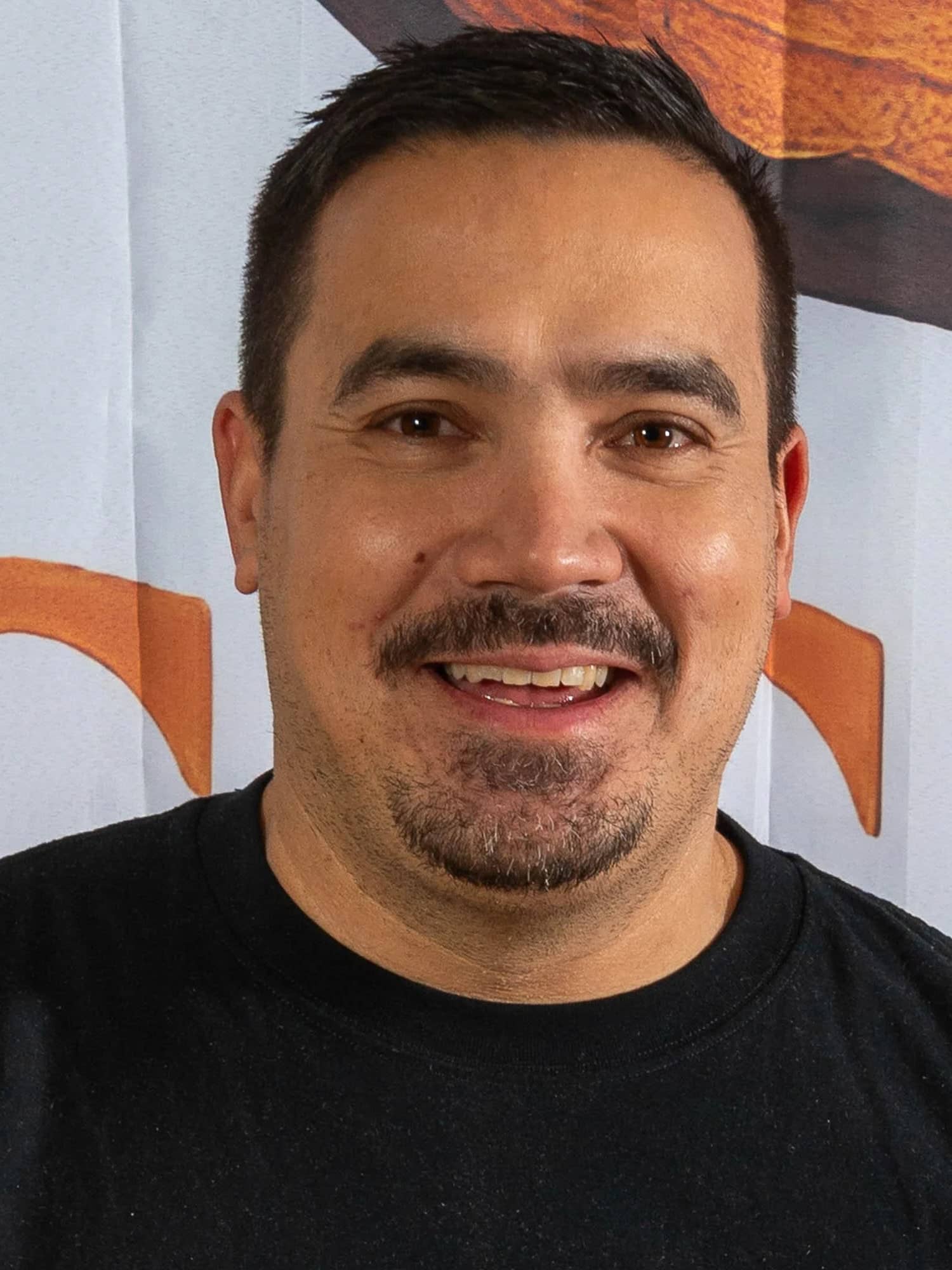 Michael Scabell, Inhaber von M. Scabell Resin Art, im schwarzen T-Shirt vor einem Banner mit orangem Motiv.