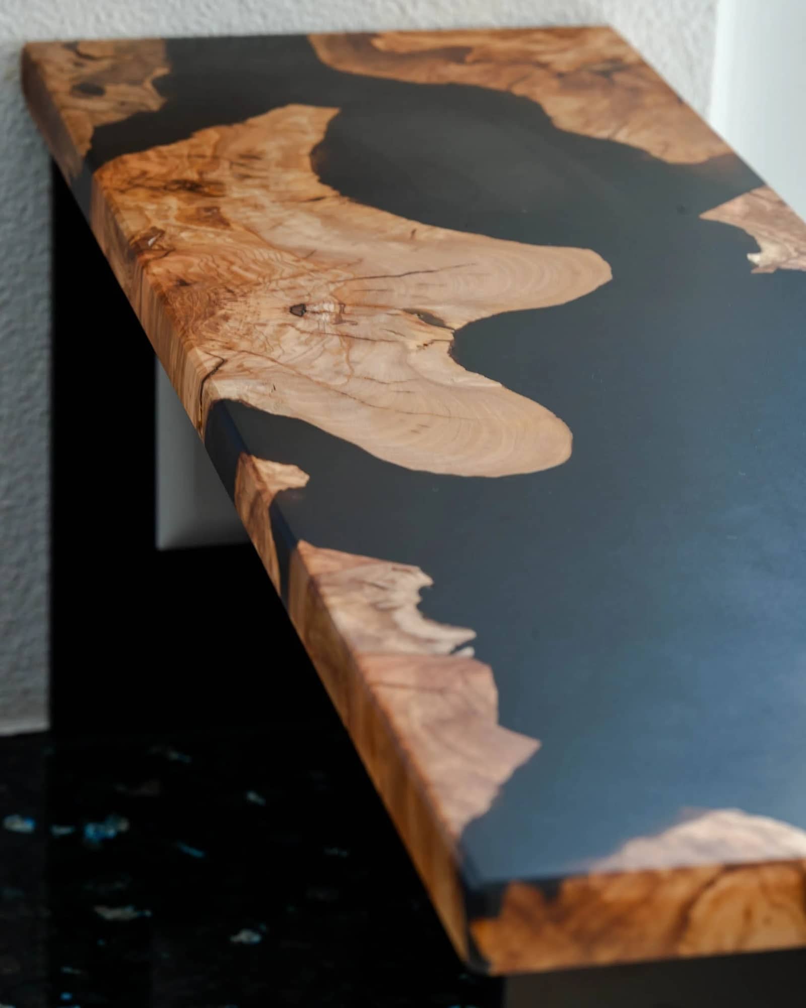 Tischplatte aus hellem Holz, die Zwischenräume sind mit schwarzem Epoxidharz ausgegossen.